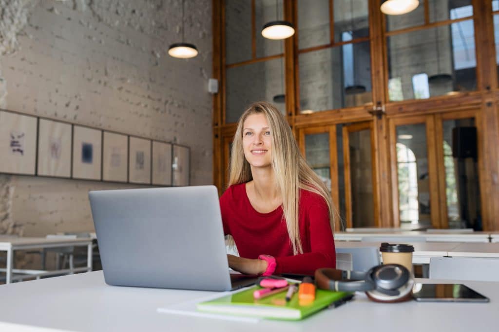 Glimlachende medewerker werkt op een laptop aan haar administratie in een lichte kantoorruimte – beeld via Magnific (magnific.com/nl/vrije-photo/externe-werknemer-online-jonge-man-aan-het-werk-op-laptop_9699500.htm)